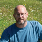 Auteur Barry Smit aan een schrijftafel in een bloemenveld.