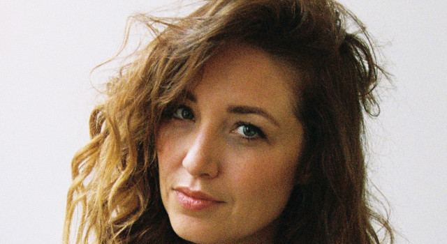 Foto van auteur Malou Holshuijsen. De draagt een witte colbert en glimlacht.