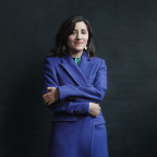 Foto van auteur Sholeh Rezazadeh. Ze draagt een wollen paarse jas en glimlacht met haar armen over elkaar naar de camera.