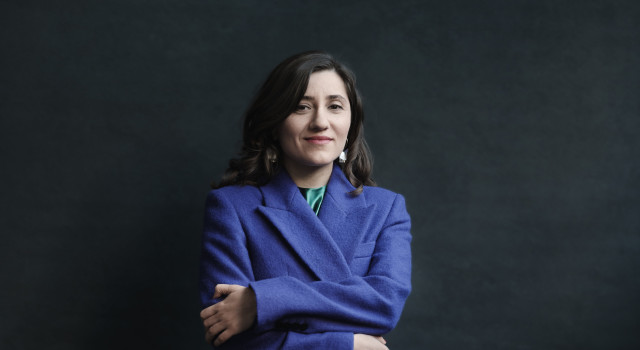 Foto van auteur Sholeh Rezazadeh. Ze draagt een wollen paarse jas en glimlacht met haar armen over elkaar naar de camera.