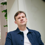 Jan van Tienen zit op een stoel en kijkt de camera in. Hij draagt een T-shirt onder een open overhemd.