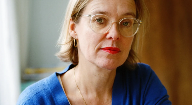 Sanneke van Hassel kijkt in de camera. Ze draagt een bril, oorbellen en een ketting.