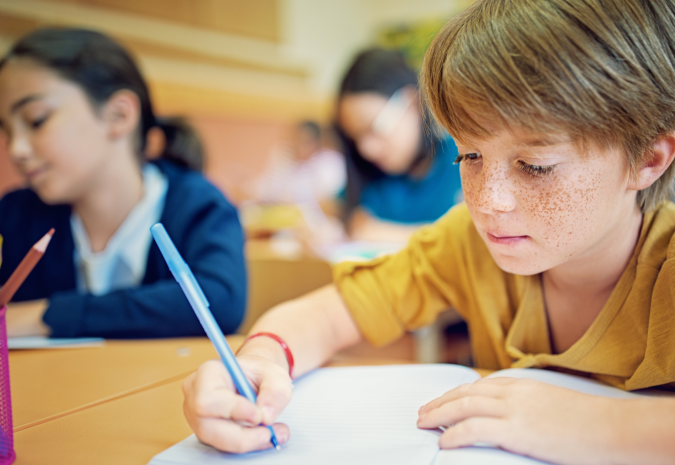 Foto van jongetje met sproeten die met een pen in een schrift schrijft