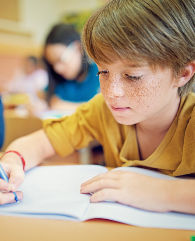 Foto van jongetje met sproeten die met een pen in een schrift schrijft